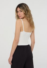 Top bianco a righe con spalline sottili, caratterizzato da una silhouette aderente e da una texture liscia, abbinato a pantaloni neri larghi.
