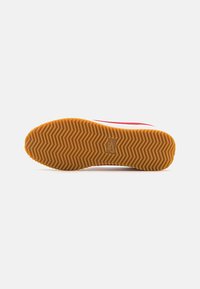 Nike-Schuhsohle mit Fischgrätenmuster, aus Gummi und in einem hellbraunen Farbton. Die Unterseite zeigt ein auffälliges Nike-Logo.