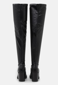 Stivali neri al ginocchio con tacco, realizzati in materiale sintetico liscio, dotati di cuciture verticali e di un tacco a blocco per garantire stabilità.
