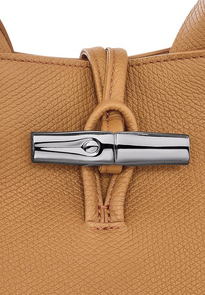 Tan leather handbag featuring a textured surface, a glossy silver clasp, and detailed stitching around the handle.