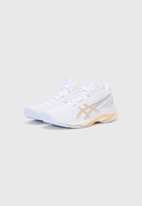 Baskets blanches de sport avec un dessus en maille respirante, des accents beige clair et une semelle en caoutchouc. Les lacets et un col rembourré améliorent l'ajustement et le confort.