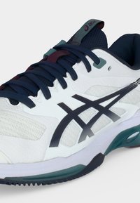 Λευκό και ναυτικό μπλε αθλητικό παπούτσι Asics με σκουρό μπλε κορδόνια, μαύρες λωρίδες λογότυπου και μαλακή σόλα με πράσινες και μαύρες λεπτομέρειες.