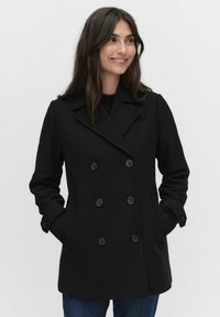 Mustan kaksirivisen villakangas takin, jossa on suuret mustat napit, terävä kaulus ja sivutaskut. Tasainen tekstuuri ja muotonsa mukaisesti istuva malli.