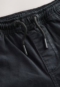 Primo piano di pantaloni neri con vita elastica e cordoncini neri infilati in occhielli metallici.