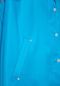 Jachetă impermeabilă albastră cu un design elegant, închidere prin capse, buzunar ascuns și o textură netedă, lucioasă.