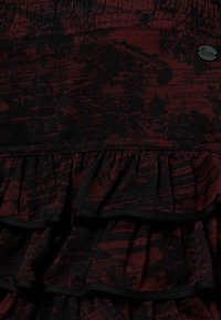 Uppblåst kjol med ett svart och mörkrött abstrakt mönster, volanglager och resårmidja. Tillverkad av mjukt, texturerat tyg.