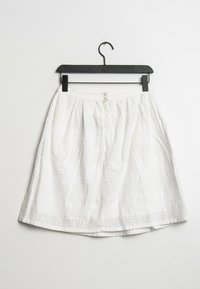 Vit kjol med horisontella öljettmönster, en samlad midja och en utsvängd silhuett. Hänger på en svart plastgalge.