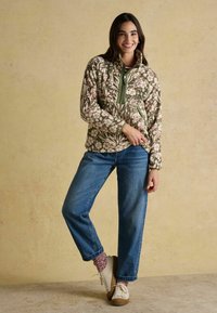 Lehká zipová bunda s zeleným květinovým vzorem spárovaná s modrými džíny. Texturovaná tkanina, vysoký límec a boční kapsy. Bílé boty.