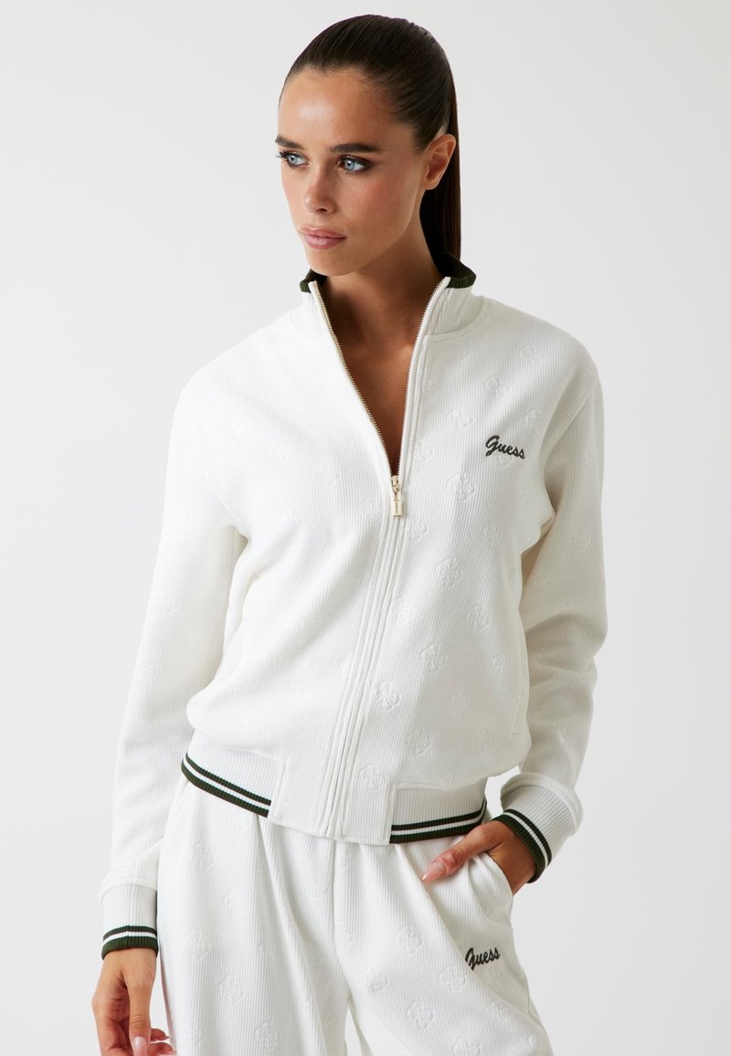 Witte zip-up jack met ribbeltextuur. Kenmerkt zich door groene gestreepte accenten op de kraag en manchetten. "Guess" logo geborduurd op de borst.