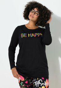 Maglietta nera a maniche lunghe con testo ricamato multicolore "SII FELICE." Abbinata a pantaloni a fantasia colorata, enfatizzando il design vivace.