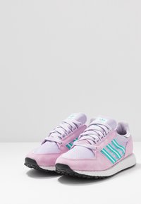 Baskets violettes et lavande avec des rayures turquoise. Fabriquées en daim et en mesh, elles présentent une semelle en caoutchouc texturée et un col rembourré.