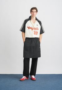 Hvit og svart kortermet skjorte med rød grafisk tekst, svart elastisk midjebånd for forkle, svarte bukser og røde sneakers med hvite striper.