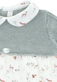 Top de punto en verde suave con un cuello blanco que presenta un patrón de animales del bosque. Sección inferior con pliegues y un acento de botón.