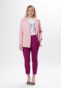 Rosa dobbeltradet blazer, hvid grafisk t-shirt med isvaffelmønster og tætsiddende magenta bukser. Sorte open-toe hæle fuldender outfittet.