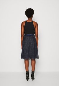 Haut sans manches noir associé à une jupe plissée bleu marine ornée de points métalliques et d'une taille lisse, le tout complété par des bottines noires.