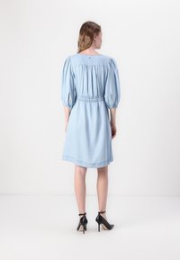 Rochie din denim bleu deschis cu mâneci bufante, talie elastică și tiv până la genunchi. Asortată cu pantofi cu toc înalt negri.
