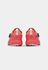 Rear view of athletic shoes with bright orange and pink gradient design, padded collar, white accents, and a circular knob for adjusting fit.