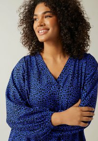 Abito autoadattante blu con motivo a stampa leopardata nera, caratterizzato da scollatura a V e maniche voluminose a palloncino con polsini arricciati.