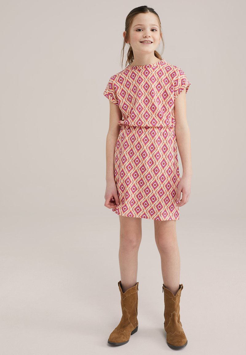 Kurzärmliges Kleid mit einem rosa-weißen Diamantmuster, tailliert, kombiniert mit braunen Cowboy-Stiefeln. Glatte Stoffstruktur.