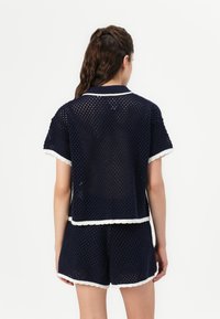 Set di pantaloni corti in rete blu navy composto da una maglietta a maniche corte con bordi bianchi e bordi ondulati, abbinata a dei pantaloni corti coordinati. Materiale in maglia testurizzata.