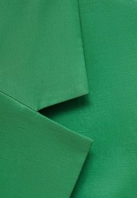 Gros plan sur un tissu vert avec un bord plié montrant la texture et le motif du tissage dans une couleur vive et unie.