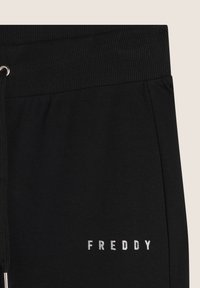 Pantaloni della tuta neri realizzati in materiale morbido con vita a costine, dotati di un logo argento "FREDDY" sul davanti. Inclusa corda di regolazione.