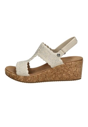Sandale compensée beige avec semelle en liège, brides en maille festonnées décorées de petites perles brillantes et bride élastique arrière.