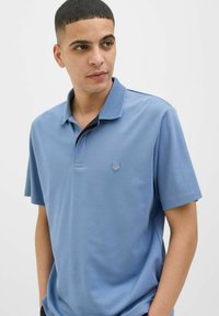 Šviesiai mėlynas polo marškinėlis su tekstūruotu apykakle, trumpomis rankovėmis, mažu emblemu kairėje krūtinės pusėje ir minkšta medžiagos tekstūra.