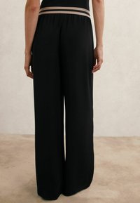 Mustad laiapõlvedega püksid pehme tekstuuriga, millel on kontrastne beež vöökoht. Lihtne, minimalistlik disain ilma täiendavate mustriteta.