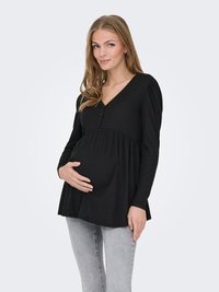 Femme enceinte portant un haut à manches longues noir et un jean gris clair, tenant doucement son ventre d'une main.