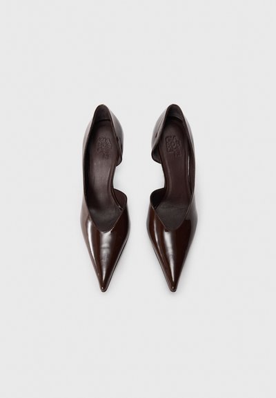 Smeđe salonke od lakirane kože šiljastog vrha sa elegantnim dizajnom i otvorenim stranicama. Unutrašnjost ima utisnutu marku. Glatki, sjajni završetak.