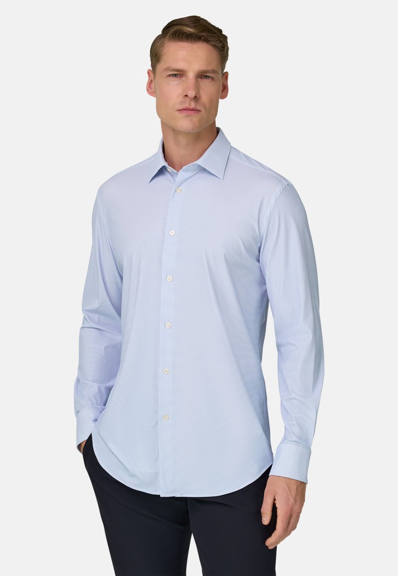 Chemise bleu clair à manches longues avec un col boutonné, présentant un motif à carreaux subtil et un ourlet arrondi. Fabriquée en tissu lisse.