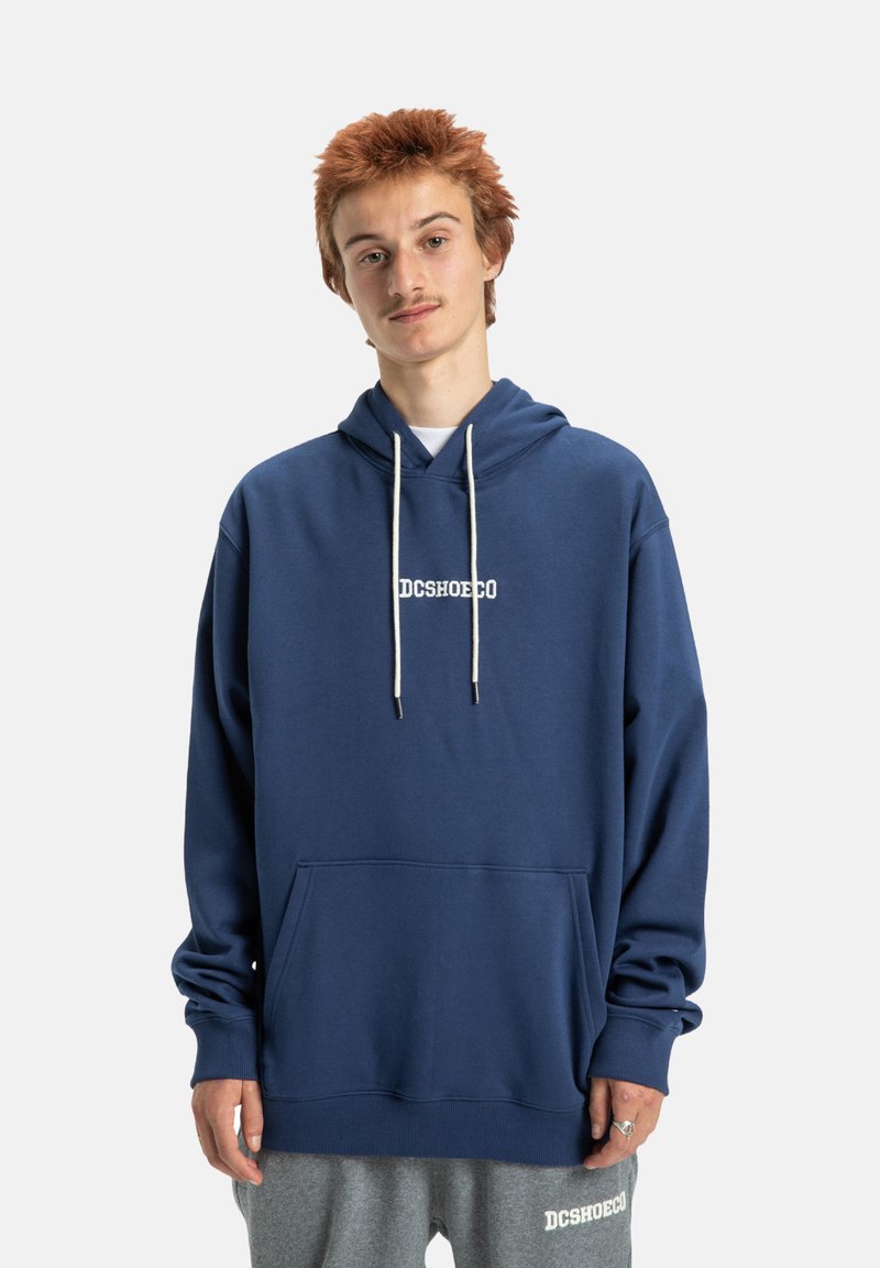 Námornícky modré mikina s kangaroo vreckom, bielymi šnúrkami a potlačou "DCSHOECO". Vyrobená z mäkkej tkaniny s voľným strihom.