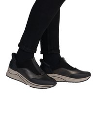 Chaussures noires à enfiler avec un mélange de cuir et de tissu, dotées d'un zip et d'une semelle en caoutchouc beige. Texture lisse et forme arrondie.