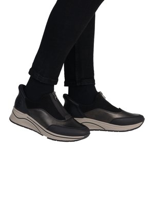 Chaussures noires à enfiler avec un mélange de cuir et de tissu, dotées d'un zip et d'une semelle en caoutchouc beige. Texture lisse et forme arrondie.