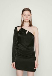 Vestido preto de um só ombro feito de material brilhante, apresentando um design drapeado e um recorte no peito. Manga longa de um lado.