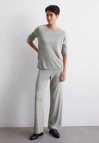 Szary sweter dziany z długimi rękawami i okrągłym dekoltem, w połączeniu z szerokimi spodniami dzianymi w tym samym kolorze. Czarne mokasyny dopełniają stylizację.