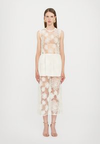Witte kanten jurk met bloemenpatronen, gelaagd over een effen witte onderlaag. Mouwloos ontwerp, kniehoogte, met een getailleerde top en een uitlopende rok.