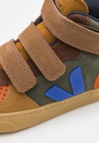 Baskets Velcro en daim marron et vert, mesh orange et accents logo bleus. Bout rond et semelle en caoutchouc avec un motif de traction texturé.