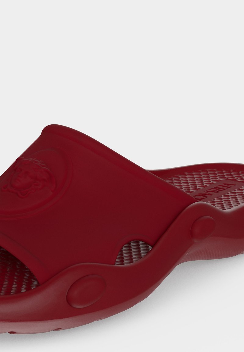 Red rubber slip-on sandal with textured footbed and embossed Medusa logo on the wide upper strap.