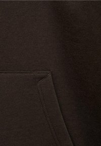 Felpa marrone con un tessuto morbido e testurizzato, dotata di tasca a canguro e cuciture a vista. Il design è minimalista e adatto per un look casual.