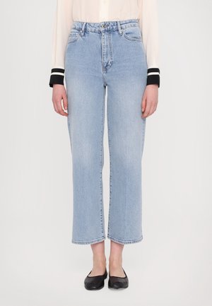 Lyseblå jeans med høj talje og lige ben, båret med sorte flade sko og en cremefarvet bluse med sorte og hvide manchetter.
