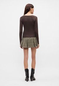 Καφέ μακρυμάνικη μπλούζα συνδυασμένη με πράσινη καρό πλισέ φούστα; στιλιζαρισμένη με μαύρες μπότες μέχρι τον αστράγαλο και σκουλαρίκια κρίκους. Λείο ύφασμα, εφαρμοστή σχεδίαση.