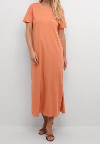 Robe maxi en tissu doux pêche, avec des manches courtes, un col rond et des fentes sur les côtés pour faciliter les mouvements.