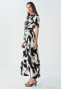 Čierno-biely maxi šaty s potlačou listov, krátkymi rukávmi, opasok v páse a voľnou siluetou. Kombinované s čiernymi sandálmi na podpätku.