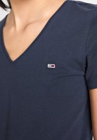 Granatowa koszulka typu V-neck wykonana z gładkiej bawełny, z małym haftowanym logo w czerwonym, białym i niebieskim kolorze na piersi.