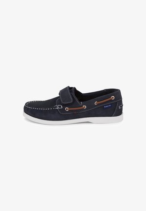 Mocasín casual de ante azul marino con costuras blancas, detalle de cordones marrones, tira de velcro y suela de goma blanca.
