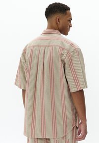 Camisa de manga corta con un patrón a rayas en beige, rojo y blanco, con un corte relajado, pliegue en la espalda y un cuello estándar.