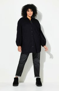 Camicia nera oversize con bottoni, maniche lunghe a sbuffo, abbinata a jeans scuri e stivaletti neri alla caviglia. Tessuto liscio.