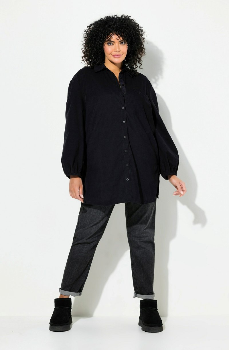 Camicia nera oversize con bottoni, maniche lunghe a sbuffo, abbinata a jeans scuri e stivaletti neri alla caviglia. Tessuto liscio.